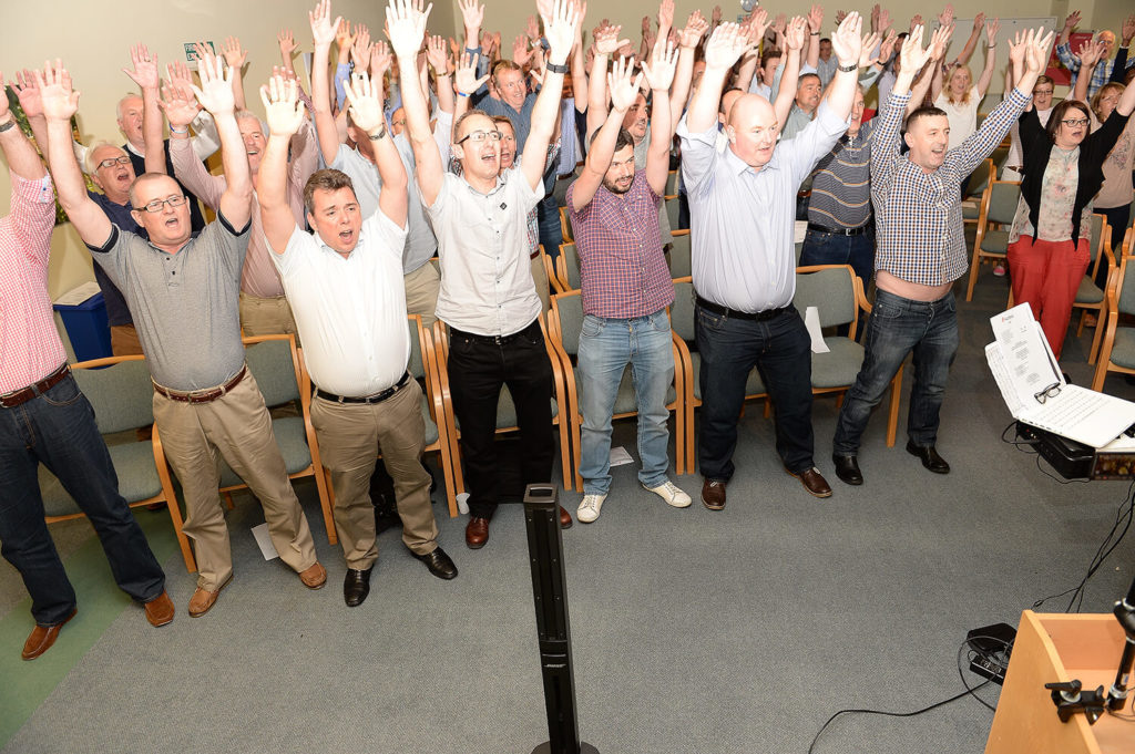 Men standing up smiling hands in the air for Body percussion conference ice breaker