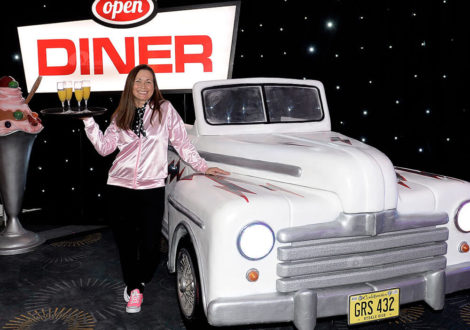 Waitress posing by Cadillac car and diner sign at themed American diner party